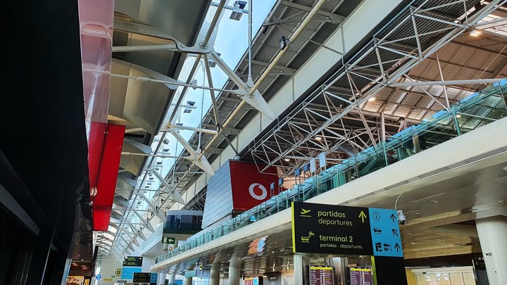 A departures sign pointing to the check-in floor and the shuttle for Terminal 2 inside Terminal 1 of Lisbon's Humberto Delgado airport, under the steel roof